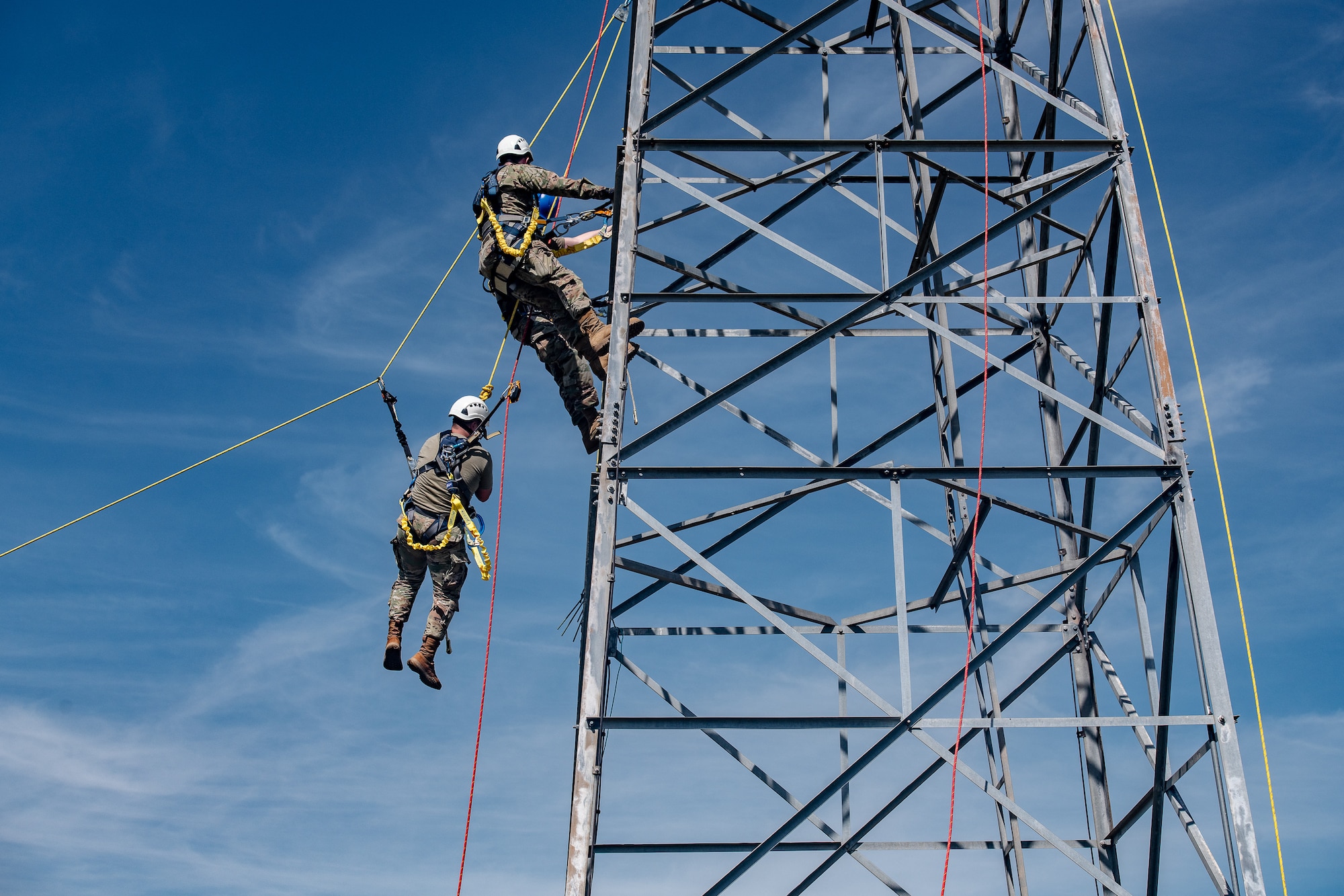 An Airman is lowered from a metal antenna tower during a rescue training scenario