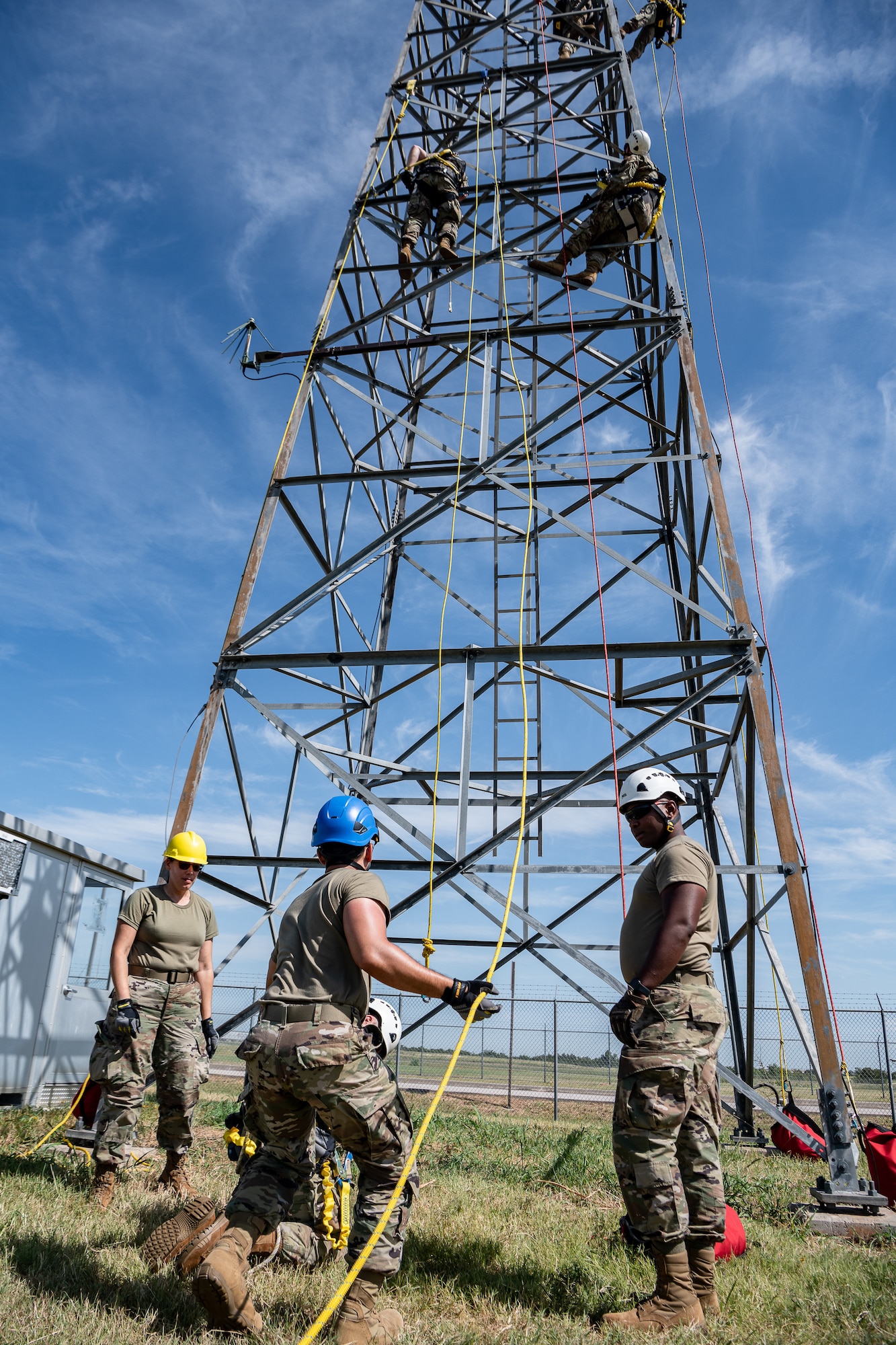 Airmen in hard hats monitor a simulated rescue from a radio tower