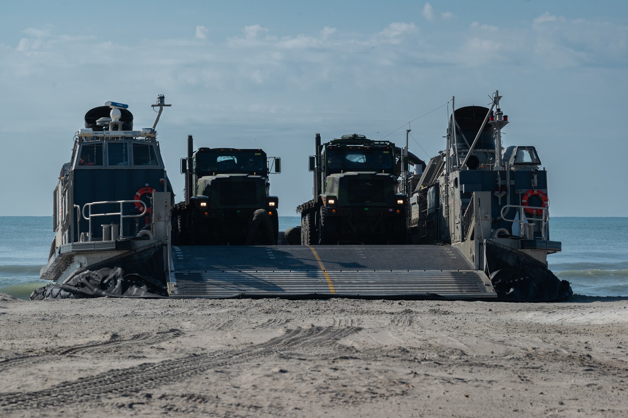 Navy Expeditionary Combat Command Seabees assigned to Naval Mobile Construction Battalion 11 and their construction vehicles are delivered to shore by U.S. Navy Landing Craft Air, Cushion (LCAC) 88 at Onslow Beach, Marine Corps Base Camp Lejeune, North Carolina, August 9, 2023,  during Large-Scale Exercise 2023 (LSE 2023). LSE 2023 demonstrates the Navy’s and Marine Corps’ ability to employ precise, lethal, and overwhelming force globally across six maritime component commands, seven numbered fleets, and 22 time zones. LSE 2023 merges real-world operations with virtually constructed scenarios to create a realistic training environment that allows Sailors and Marines to train how they will fight, regardless of geographic boundaries. (U.S. Air Force photo by Airman 1st Class Rebecca Sirimarco-Lang)