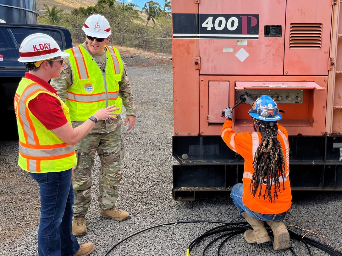 Three people in safety vests and hard hats work on a temporary power generator.