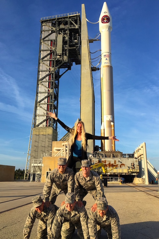 A person stands on top of a human pyramid, consisting of several uniformed service members.