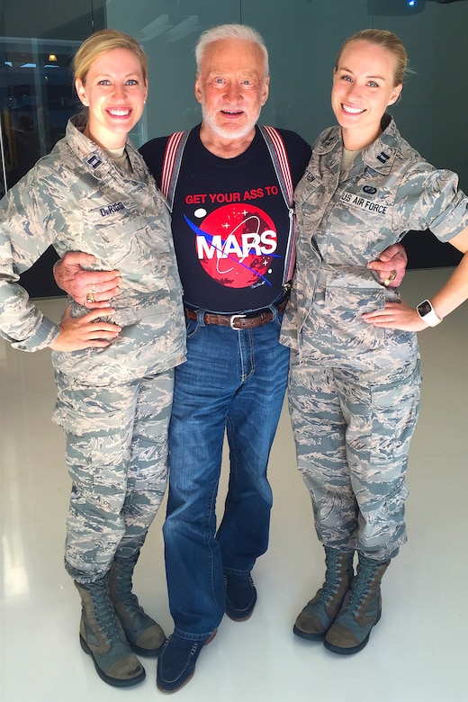 Two uniformed service members pose for a photo with an older person in civilian attire.