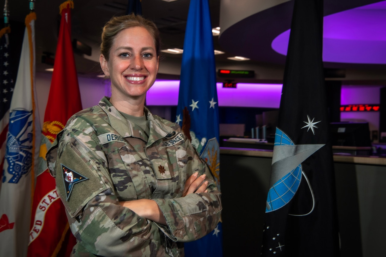 A uniformed service member smiles for a photo in front of several flags.