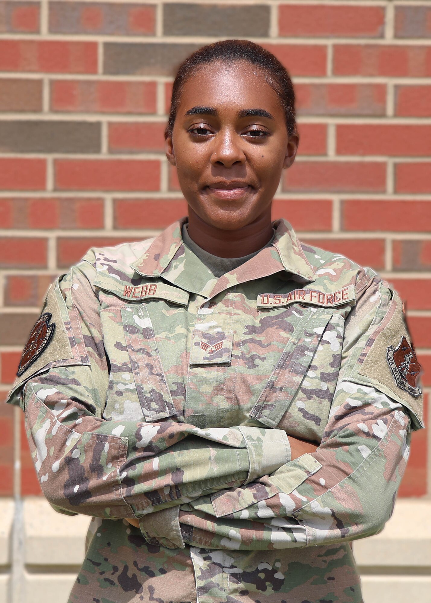 Airman stands with crossed arms in front of brick wall.