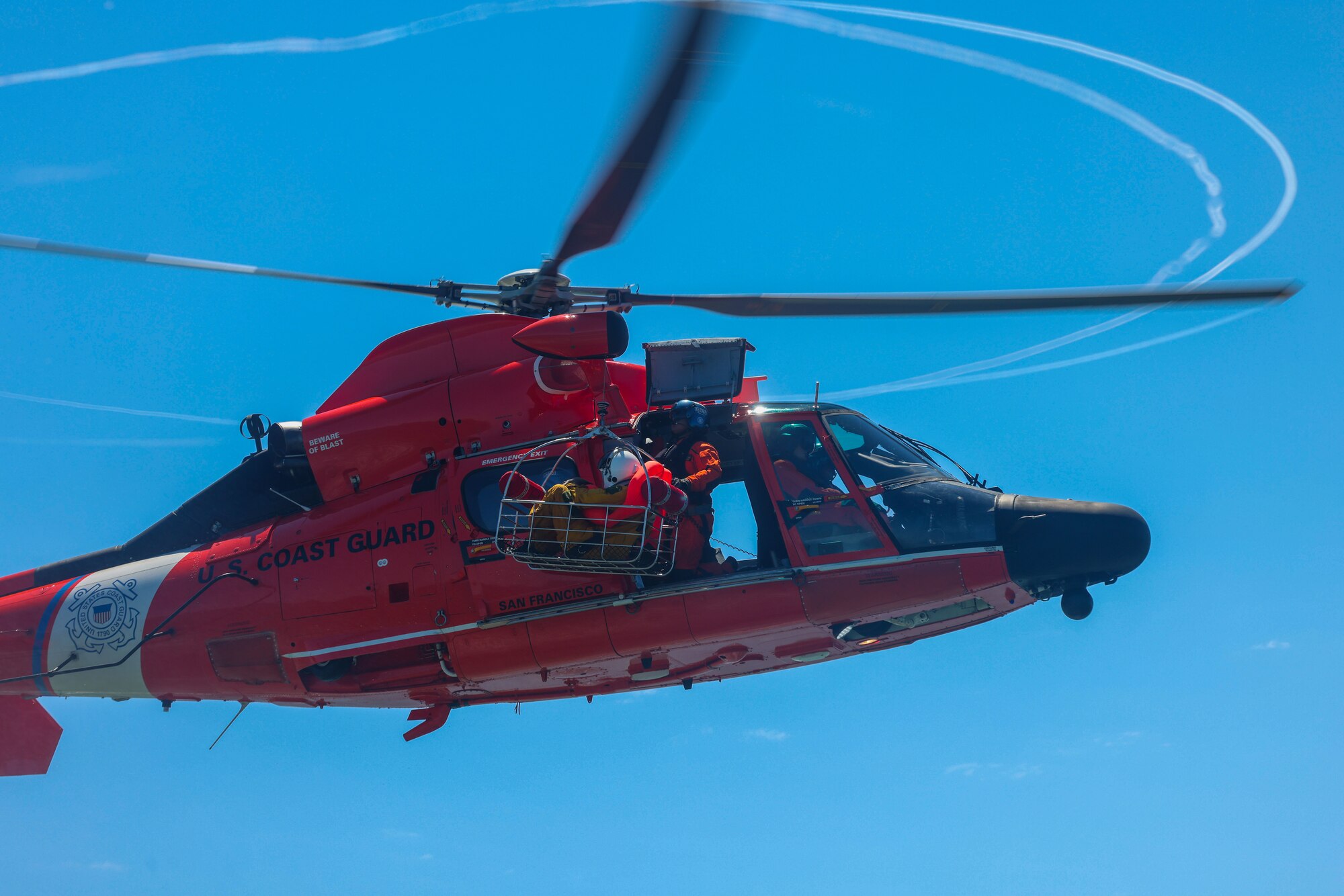 U.S. Air Force Capt. Kyle Carver, U-2 Pilot, 99 Reconnaissance Squadron, waits in the rescue basket while the U.S. Coast Guard San Francisco Sector Search and Rescue (SAR) team prepares to bring him aboard the Eurocopter MH-65 Dolphin above the San Francisco Bay, California on Aug.17, 2023.