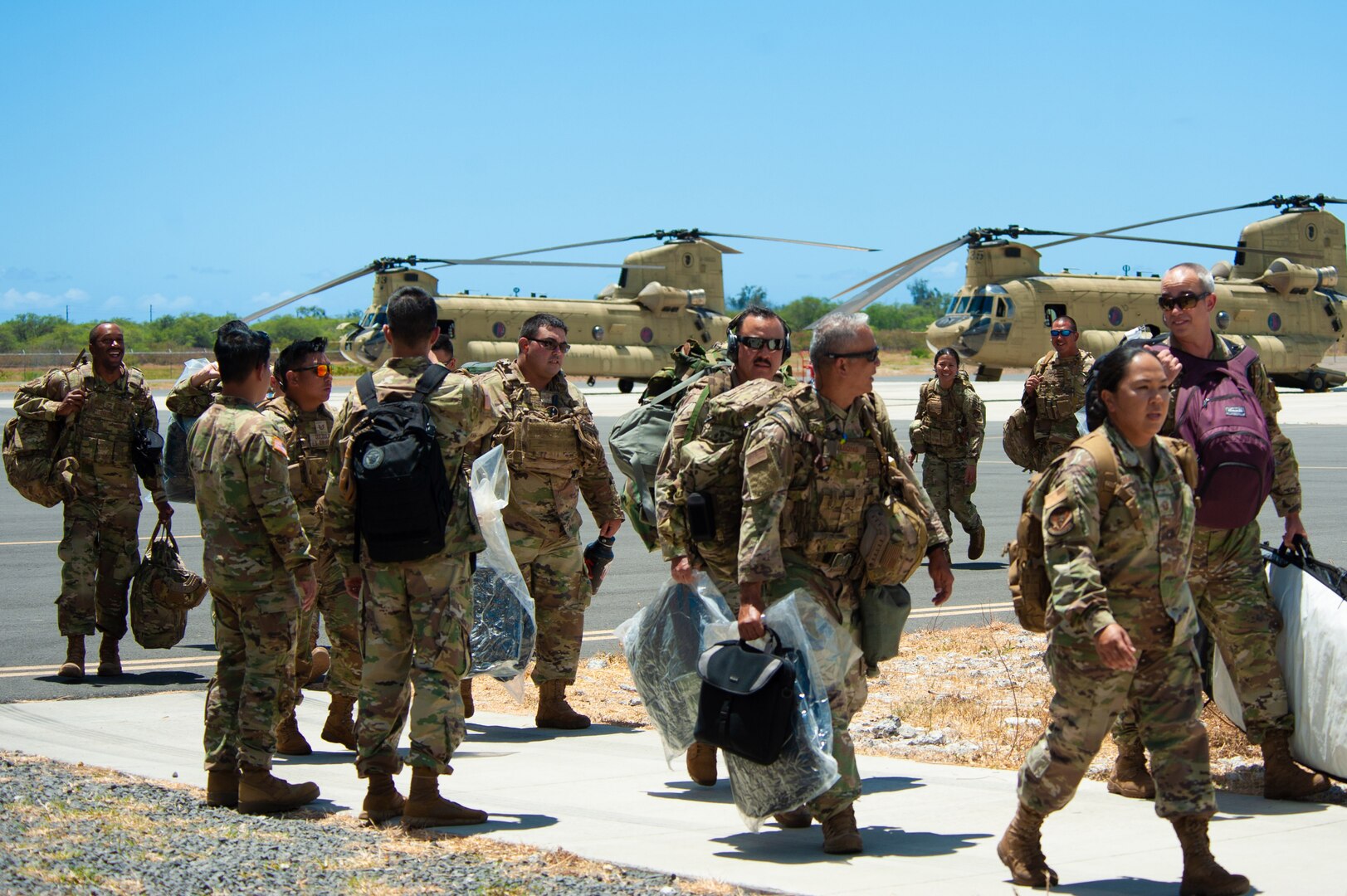 A group of service members carry packs as they walk away from two helicopters.