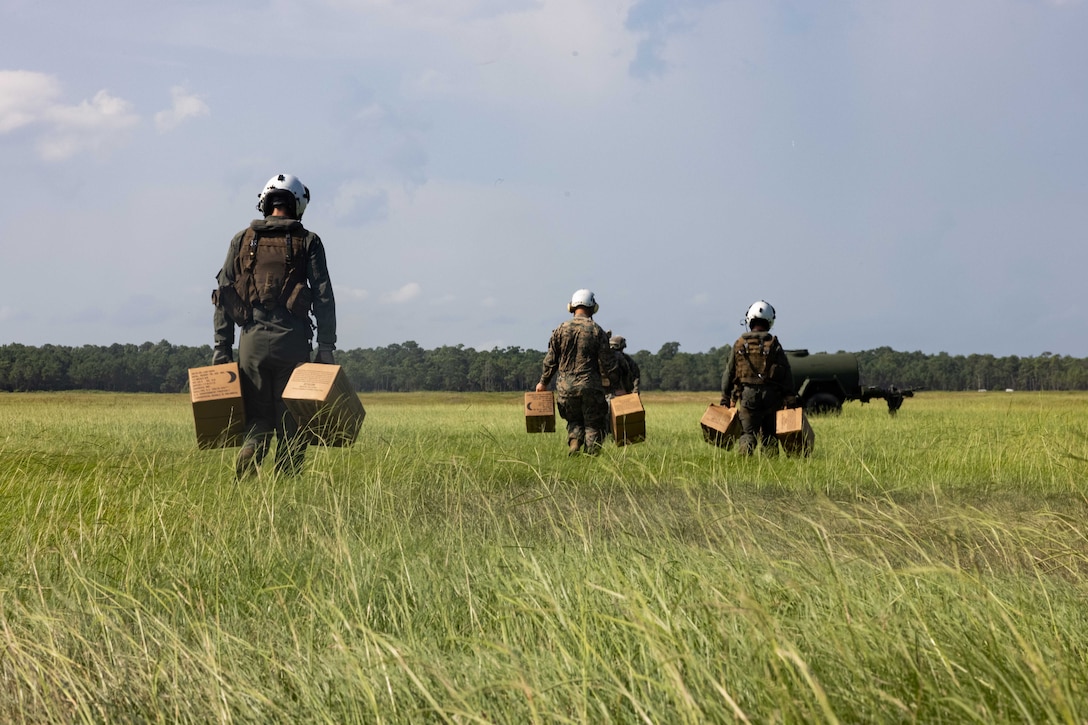 Marine carry boxes through a field.