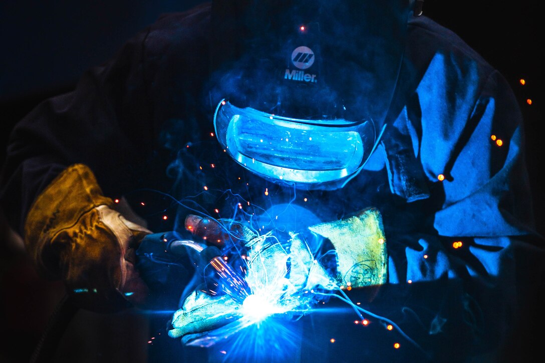 An airman wearing a helmet uses a tool to weld metal.