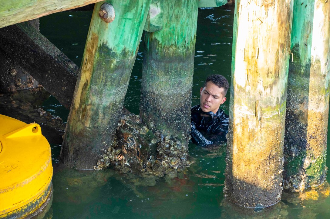 A soldier inspects a pier while moving in chest deep water.