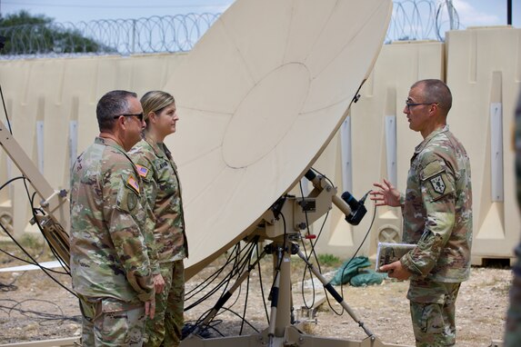 Three Soldiers stand in front of a satellite dish.