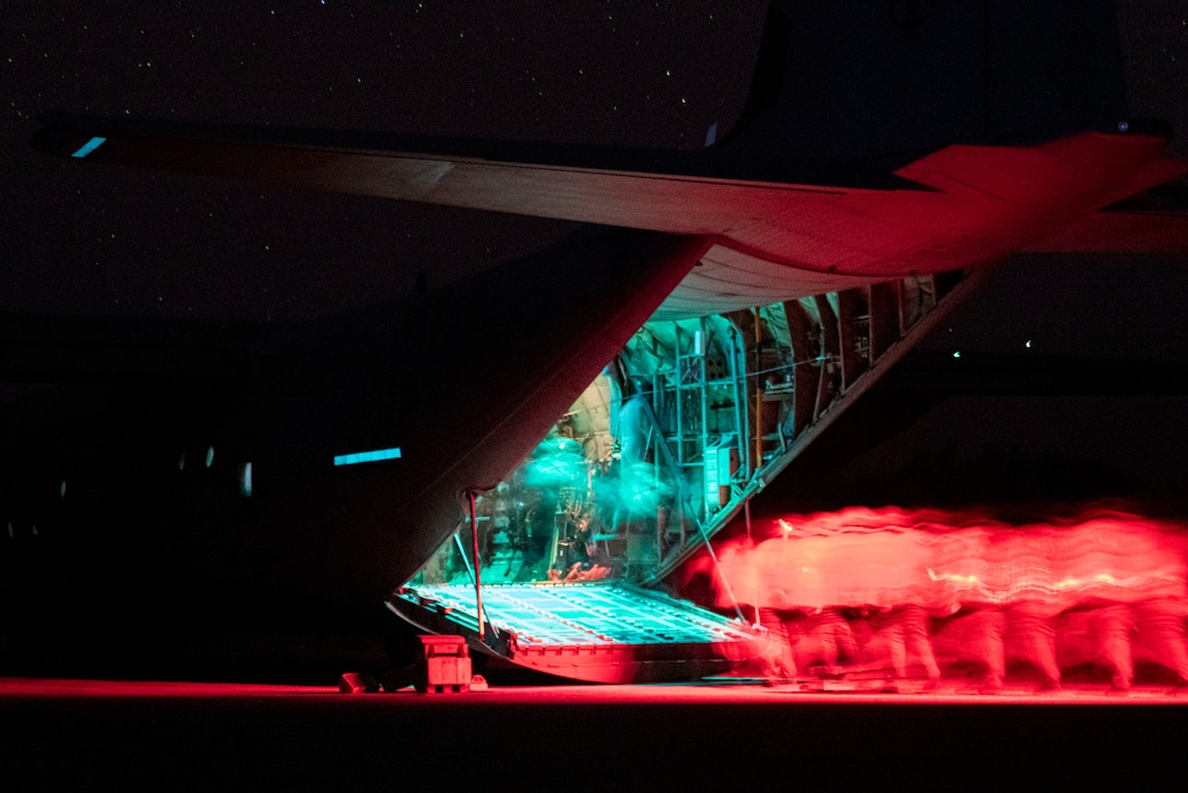 Nighttime photo of blurred individuals boarding an aircraft. The people are illuminated by red and blue lights.