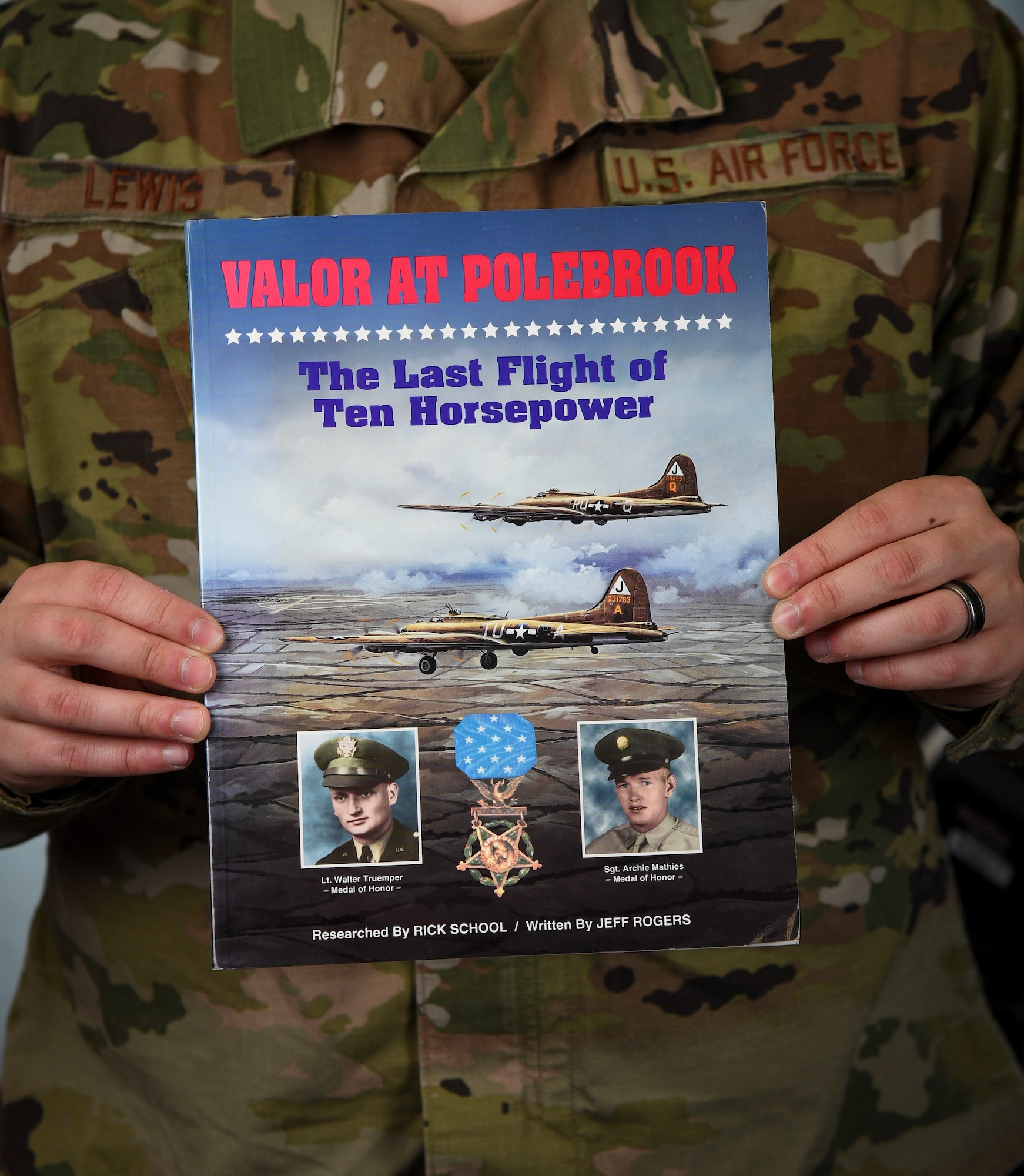 Military member holds a book close to his chest for a photo.