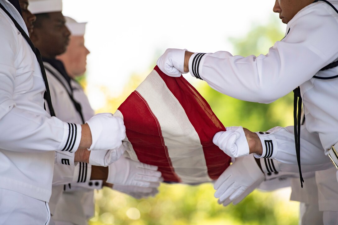A close-up of sailors in ceremonial uniforms folding an American flag.