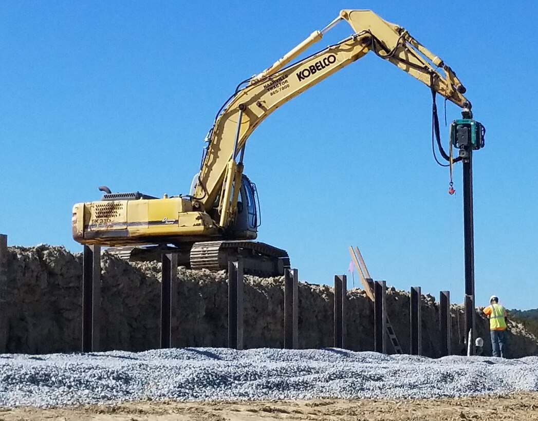 A berm wall of a mobile armor target is being constructed with steel h-piles and wooden railroad ties.