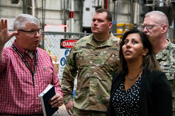 Two civilians and two military officers receive a tour of a warehouse.