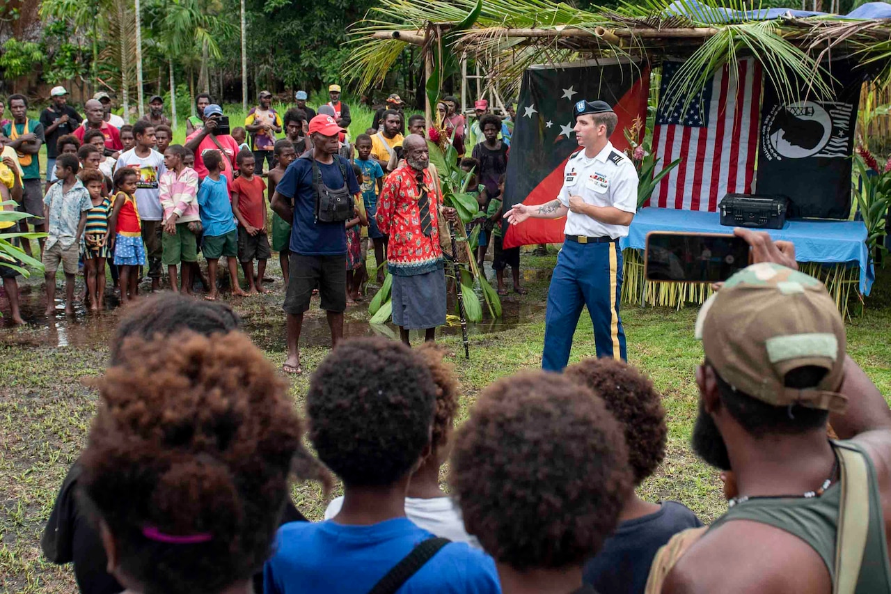 A soldier speaks to natives in a tropical area.