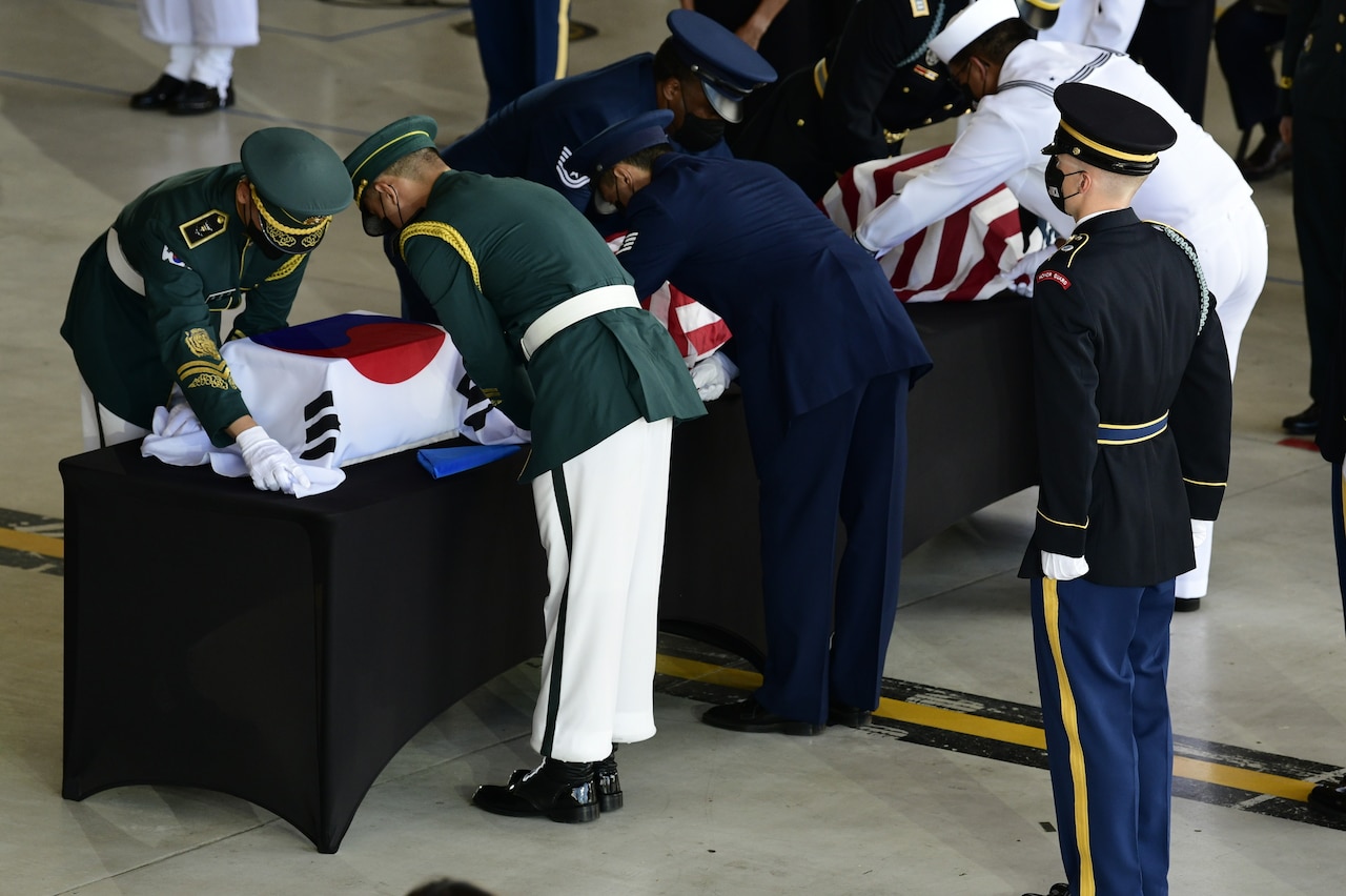 Military members honor flag-covered boxes during a repatriation ceremony.