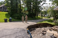 Photo of Tech. Sgt. Brandon Matott (left), 158th Fighter Wing Security Forces personnel, and Senior Master Sgt. Matthew Powell, 158th Cyber Operations superintendent, walking along a damaged roadway caused by historic flooding, during the Liaison Officer Mission, in Brookfield, Vermont, July 19, 2023. The purpose of the Liaison Officer mission is to meet with town leaders and report information from the town back to the state for possible resourcing. (U.S. Air Force photo by Tech. Sgt. Richard Mekkri)
