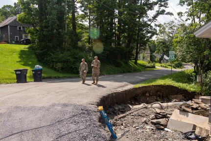 Photo of Tech. Sgt. Brandon Matott (left), 158th Fighter Wing Security Forces personnel, and Senior Master Sgt. Matthew Powell, 158th Cyber Operations superintendent, walking along a damaged roadway caused by historic flooding, during the Liaison Officer Mission, in Brookfield, Vermont, July 19, 2023. The purpose of the Liaison Officer mission is to meet with town leaders and report information from the town back to the state for possible resourcing. (U.S. Air Force photo by Tech. Sgt. Richard Mekkri)