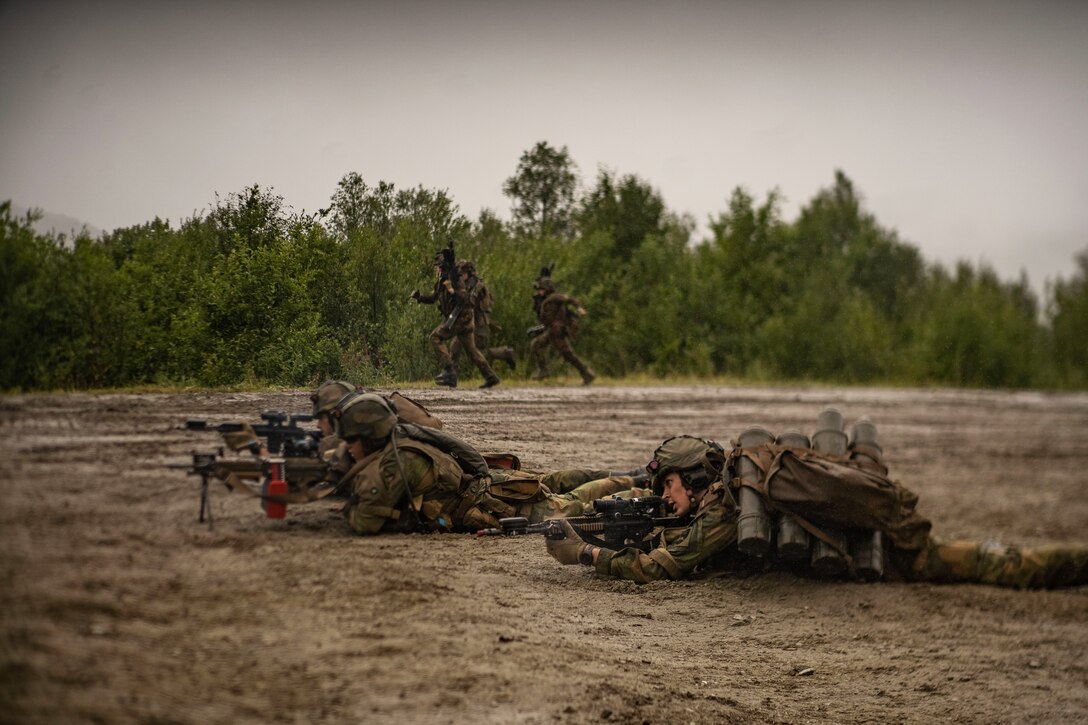 Three soldiers lie on the ground holding weapons.