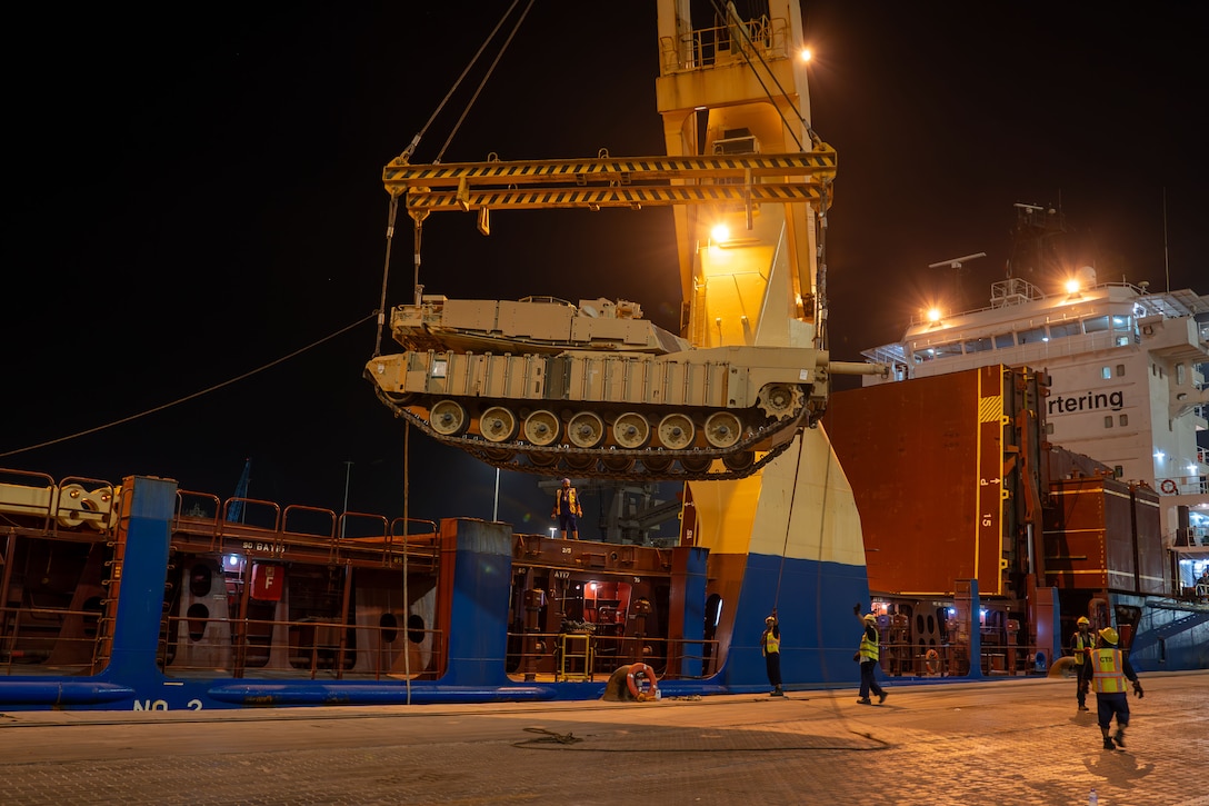 A tank is lifted into the air by cables at night.