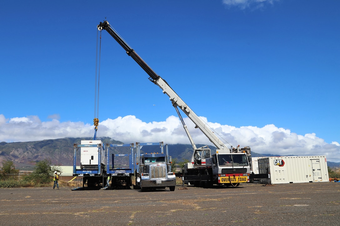 A large crane lefts a generator onto the back of a truck.