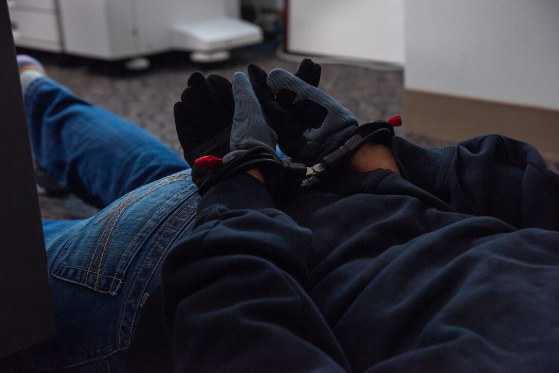 Close up of hands in handcuffs behind the back of person wearing blue jeans and blue shirt.