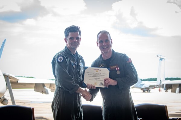 Two pilots hold an award certificate in front of jets