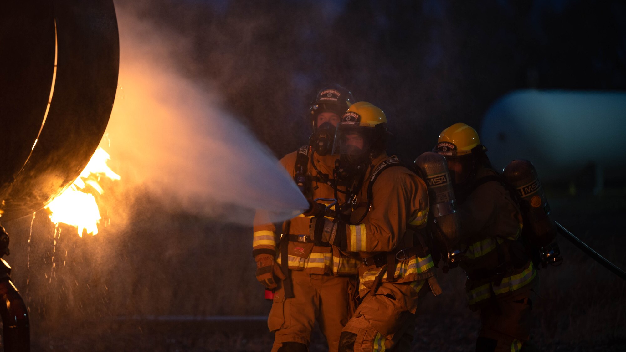 A group of 5th Civil Engineer Squadron fire protection specialists extinguish an ongoing fire during a live jet fire exercise at Minot Air Force Base, North Dakota, Aug. 21, 2023. The purpose of live burn training is to maintain readiness and give fire protection service members a realistic experience of fire before charging into an emergency situation. (U.S. Air Force photo by Airman 1st Class Alexander Nottingham)