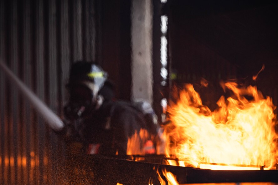 A 5th Civil Engineer Squadron fire protection specialist makes entry during a live structure fire exercise at Minot Air Force Base, North Dakota, Aug. 21, 2023. The purpose of live burn training is to maintain readiness and give fire protection service members a realistic experience of fire before charging into an emergency situation. (U.S. Air Force photo by Airman 1st Class Alexander Nottingham)