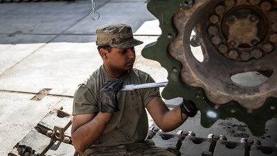 A male soldier uses a tool to work on a tank