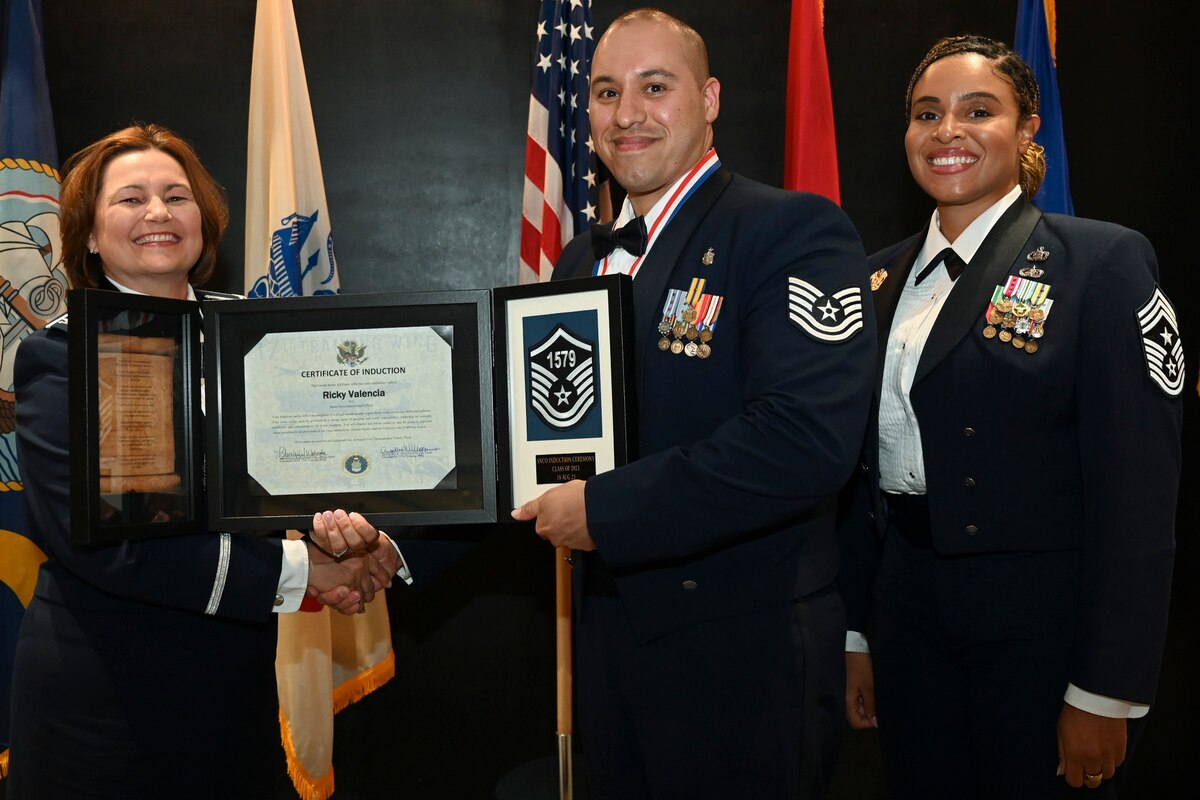 U.S. Air Force Col. Angelina Maguinness, 17th Training Wing commander, Chief Master Sgt. Khamillia Washington, 17th Training Wing command chief, and Master Sgt. Select Ricky Valencia, 17th Healthcare Operations Squadron flight chief of diagnostics and therapeutics pose for a photo at the Senior Noncommissioned Officer Induction Ceremony at the Powell Event Center, Goodfellow Air Force Base, Texas, Aug. 18, 2023. Inductees were presented a medallion, and tri-fold plaque to commemorate their achievement of reaching the highest rank tier of the enlisted force. The plaque that inductees received included their certificate, the Sergeant’s Creed, and their master sergeant insignia line number. (U.S. Air Force photo by Airman 1st Class Evelyn D’Errico)
