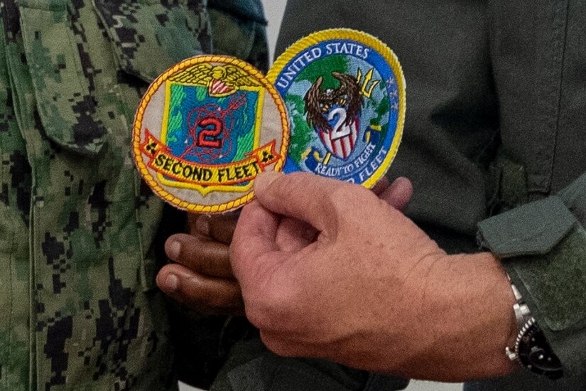 Close-up of a sailor's hand holding up two round patches for the U.S. 2nd Fleet.