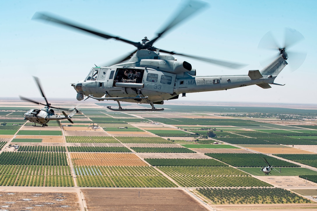 Helicopters fly above flat fields.