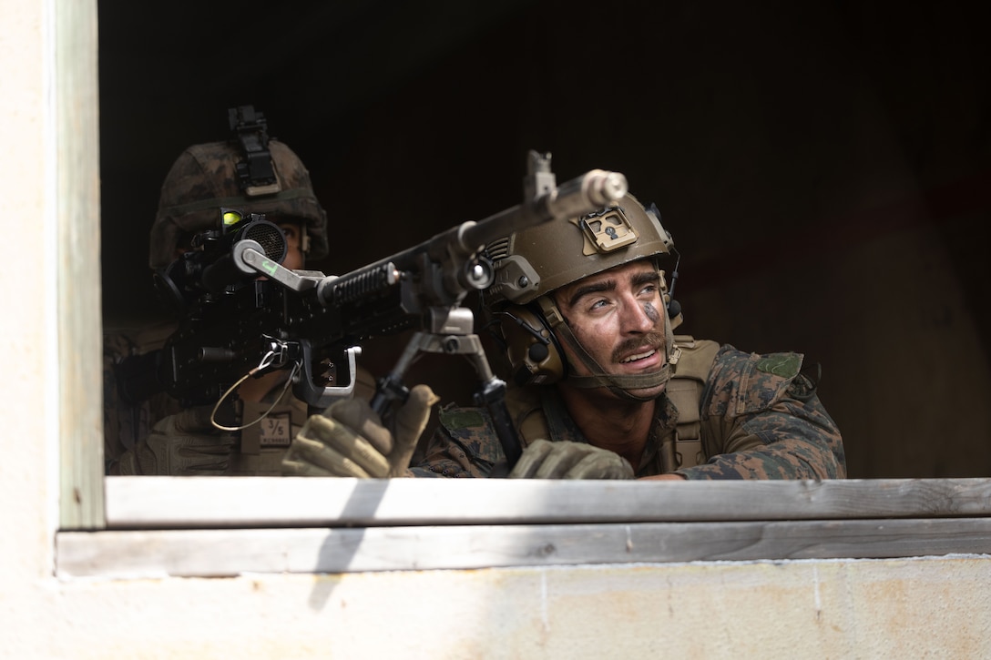 Marines fire a machine gun from a window.