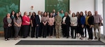 Group of people pose for a photo in open area with white walls and floor, and black mat on floor.