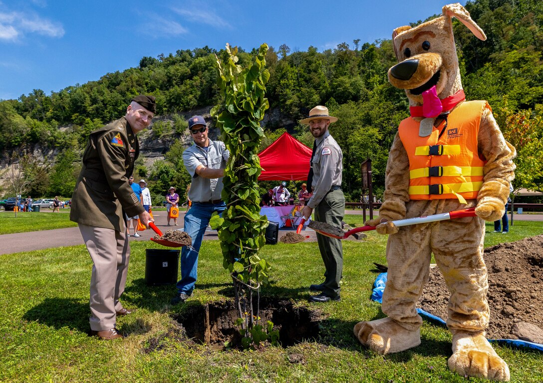 Pittsburgh District Commander Nicholas Melin, Supervisory Natural Resource Specialist Vince Klinkner, and Corps of Engineers mascot Bobber the Water Safety Dog prepare to plant a tree during a dedication ceremony at Youghiogheny River Lake’s 75th celebration in Confluence, Pennsylvania on Aug. 19, 2023