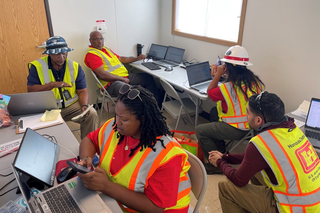 Five people in hardhats and safety vests work in an office