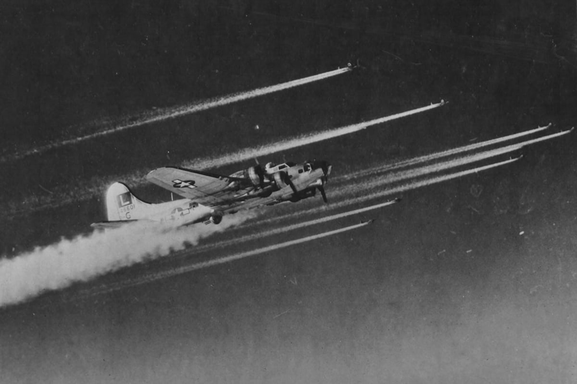 A black and white photo in which a B-17 flies in formation