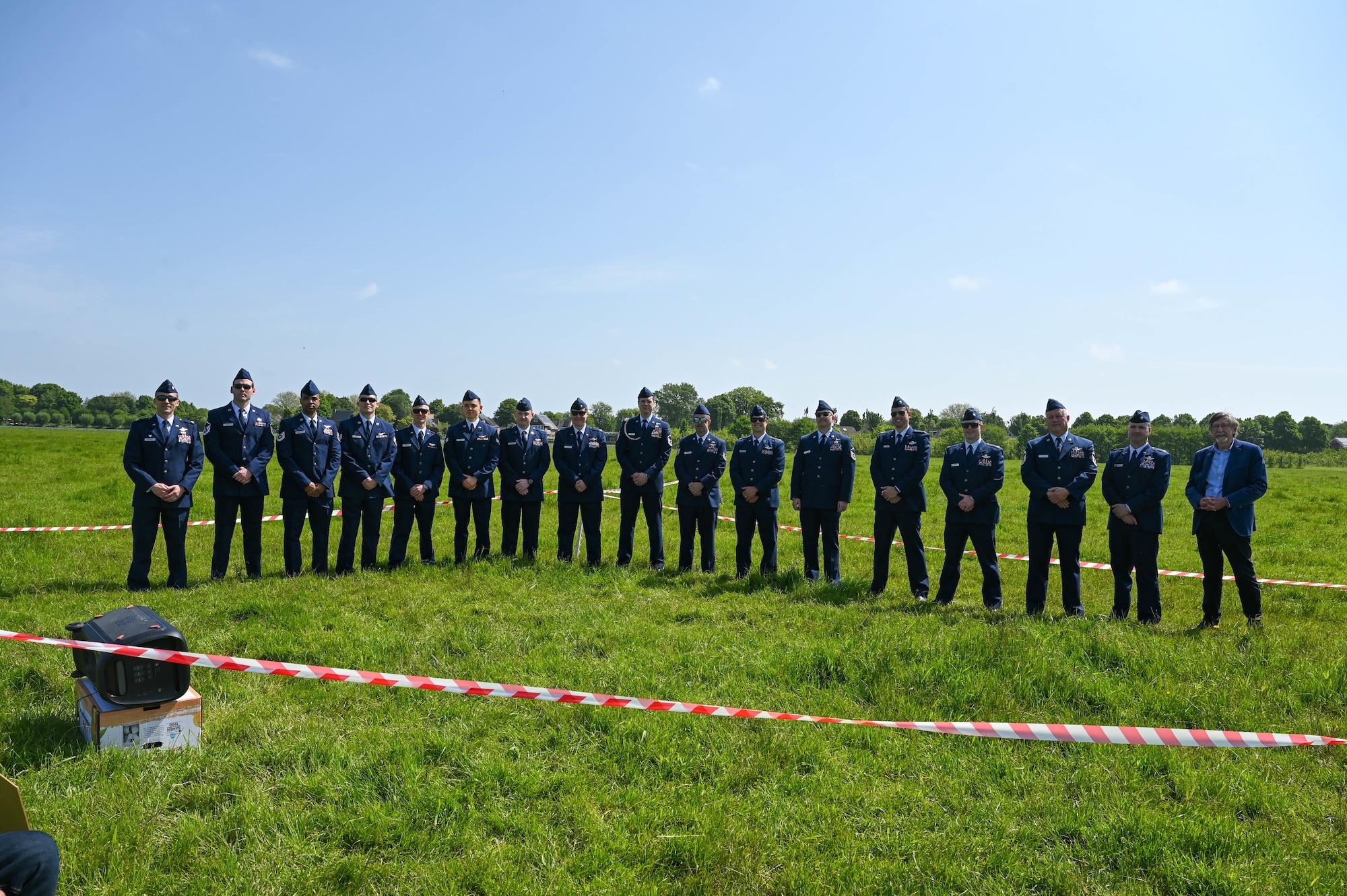 A group of men in their dress blue uniform stand in a line on a sectioned off area in a green field of grass