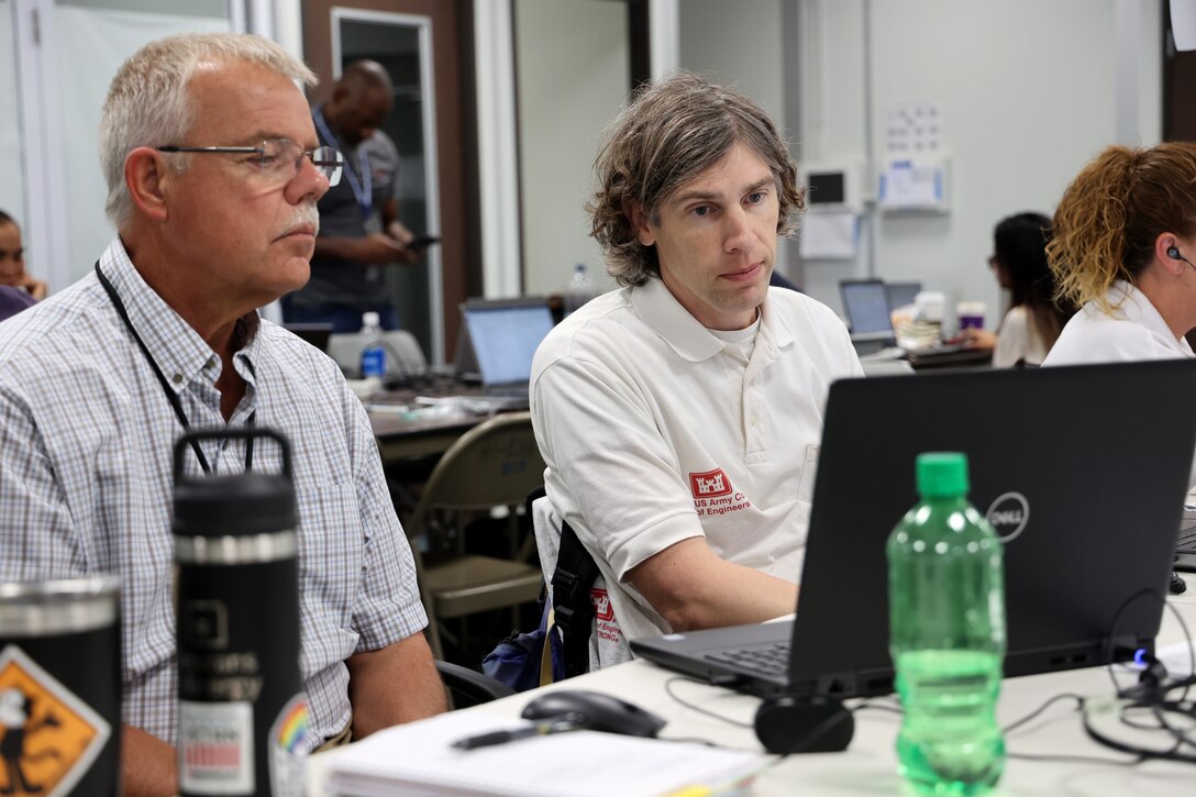 Two men are seated at a table looking at a computer screen.