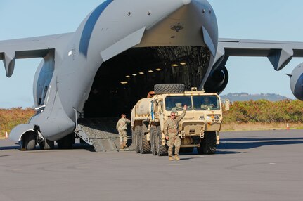 A military vehicle rolls out of the back of a military aircraft.