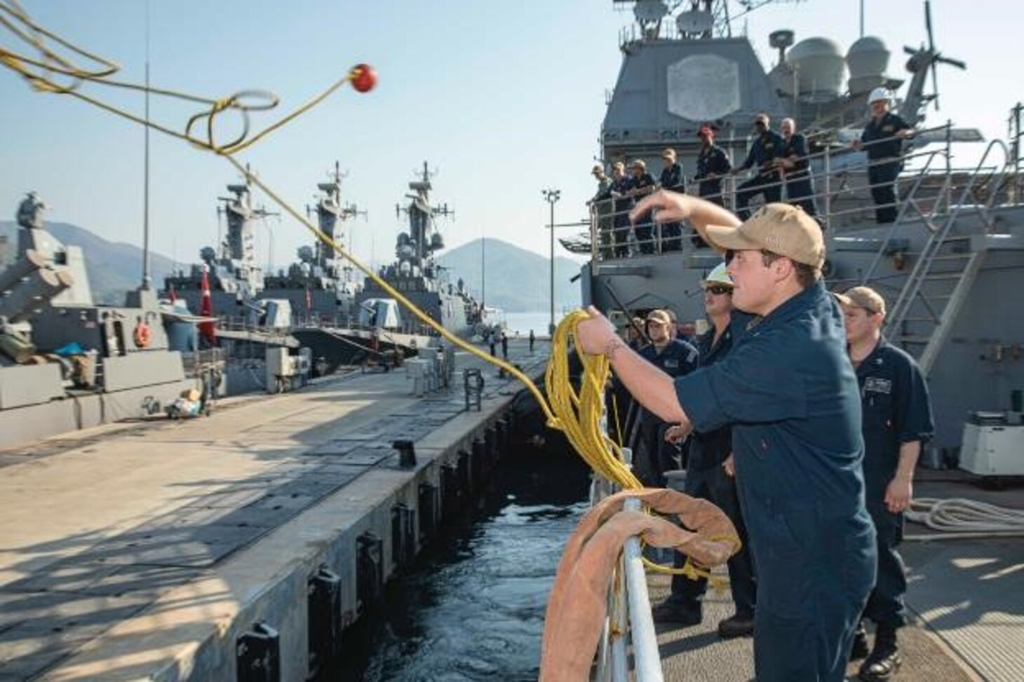 Fire Controlman (AEGIS) 3rd Class Nathan Warren, assigned to the Ticonderoga-class guided missile cruiser USS Normandy (CG 60), throws a heaving line to the pier, as the ship pulls in Aksaz Naval Base, Turkiye, Aug. 26, 2023. Normandy is part of the Gerald R. Ford Carrier Strike Group and is on a scheduled deployment in the U.S. Naval Forces Europe area of operations, employed by Sixth Fleet to defend U.S., allied, and partner interests. (U.S. Navy photo by Mass Communication Specialist 2nd Class Malachi Lakey)