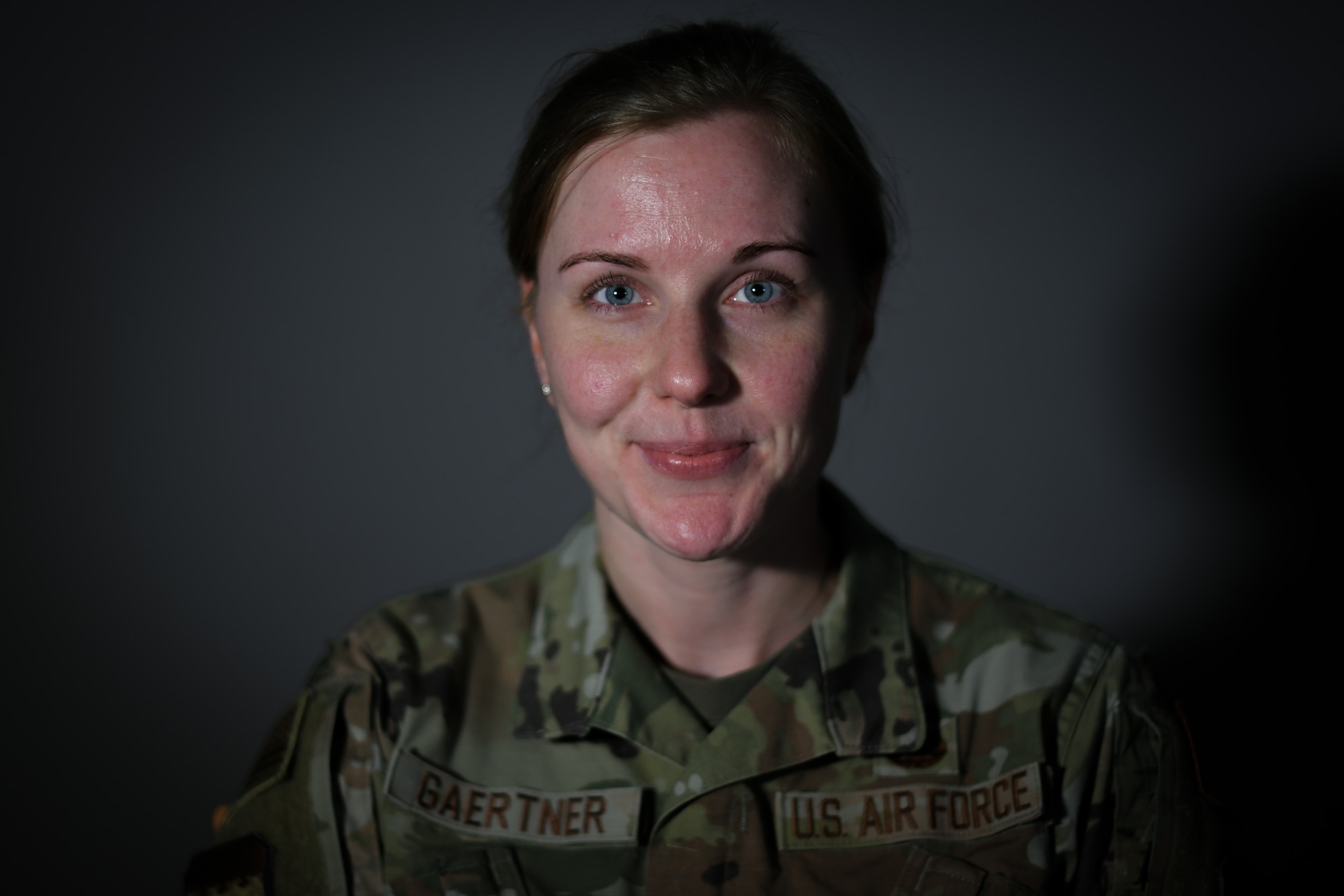 Military member poses for a photo against dark grey background.