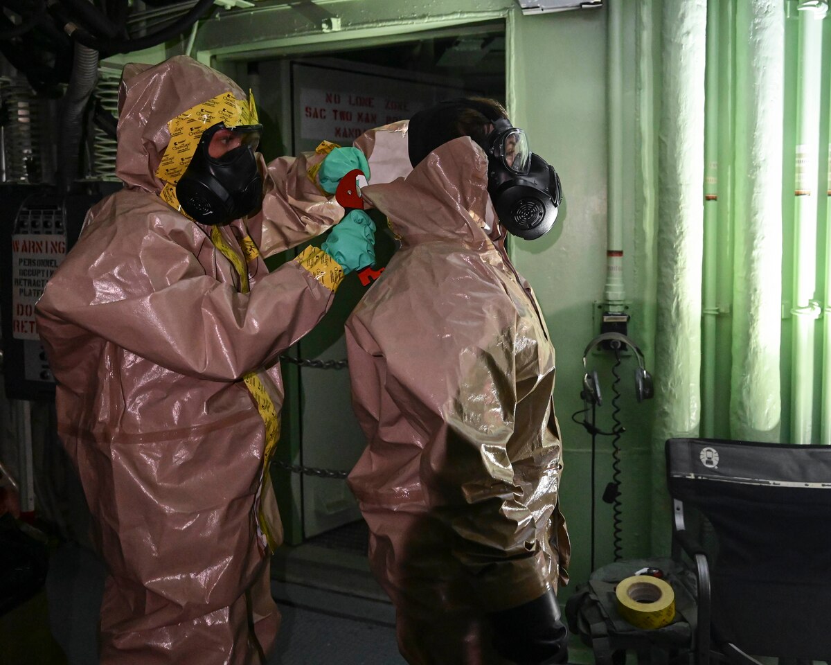 Woman in chemical suit cuts co-worker out of her chemical suit.