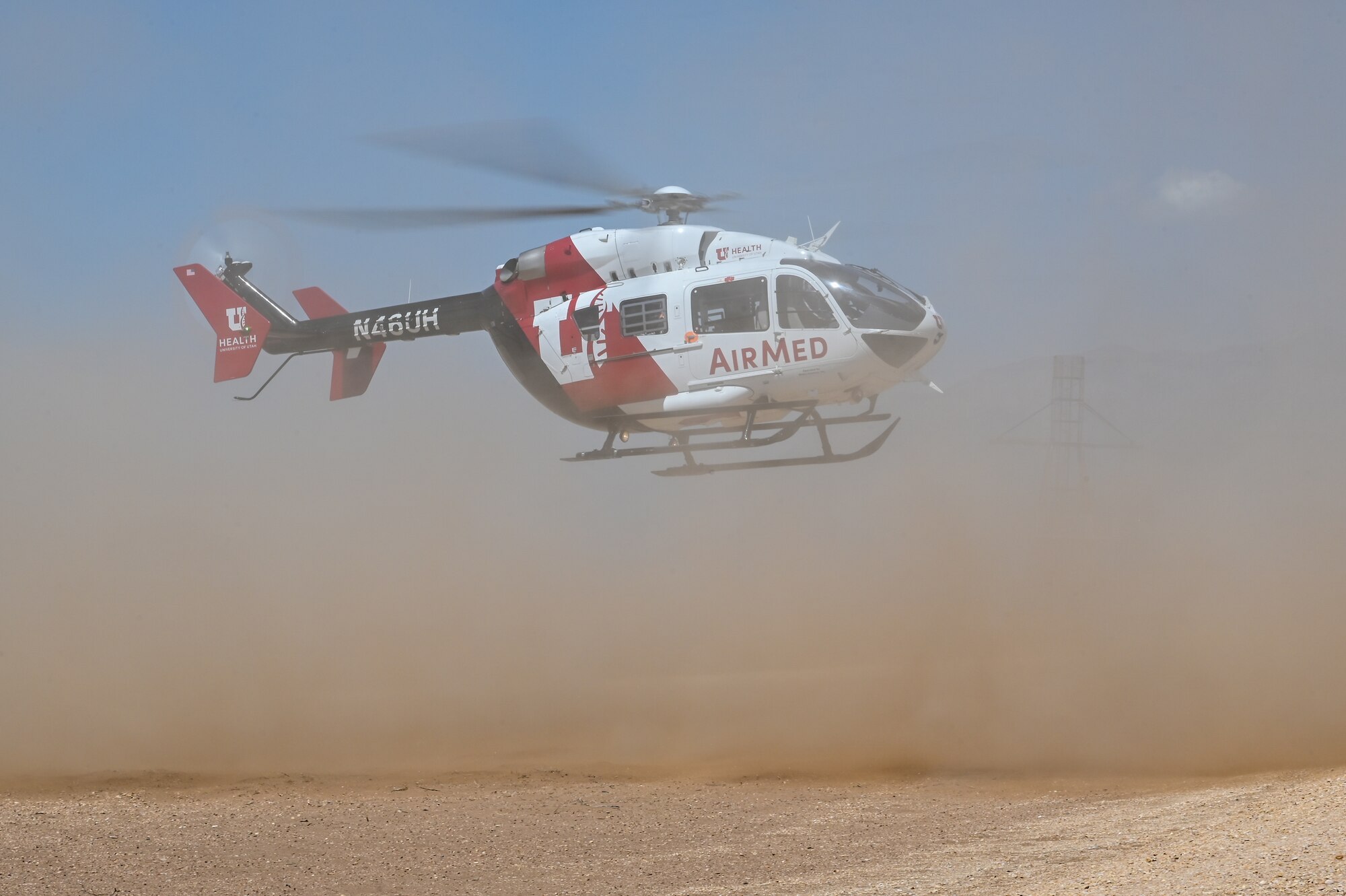 A red and white U of U AirMed helicopter lands in a dusty field on Hill Air Force Base