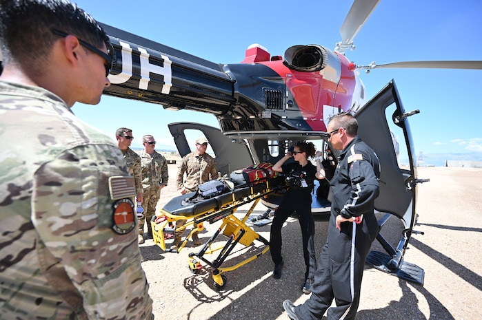 People stand around a helicopter in a dusty field conducting emergency training.