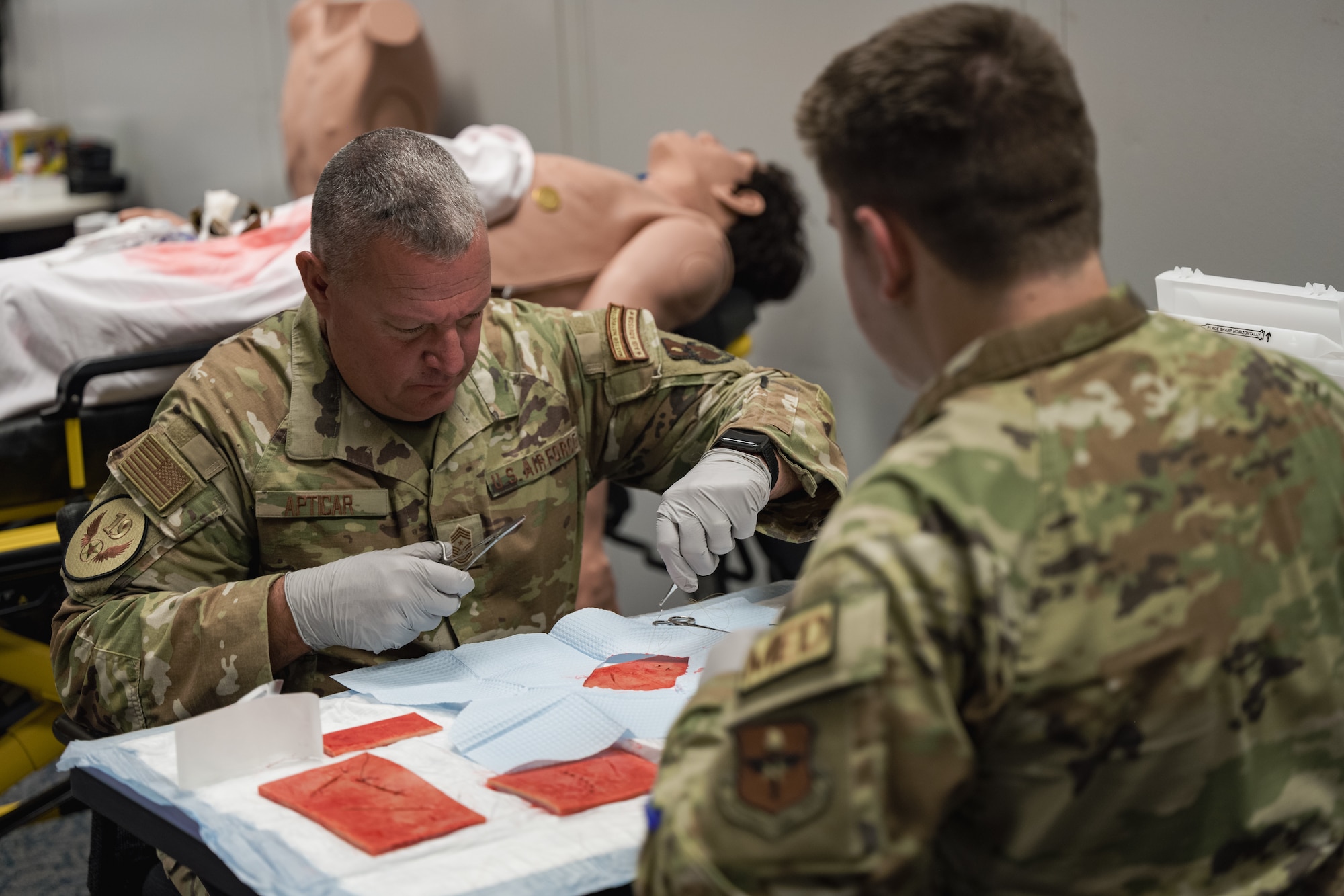 U.S. Air Force Chief Master Sgt. Justin Apticar, 19th Air Force command chief, left, learns how to properly suture a wound at Holloman Air Force Base, New Mexico, Aug. 22, 2023.