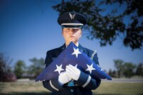 A woman in ceremonial uniform holds a folded U.S. flag in white-gloved hands.