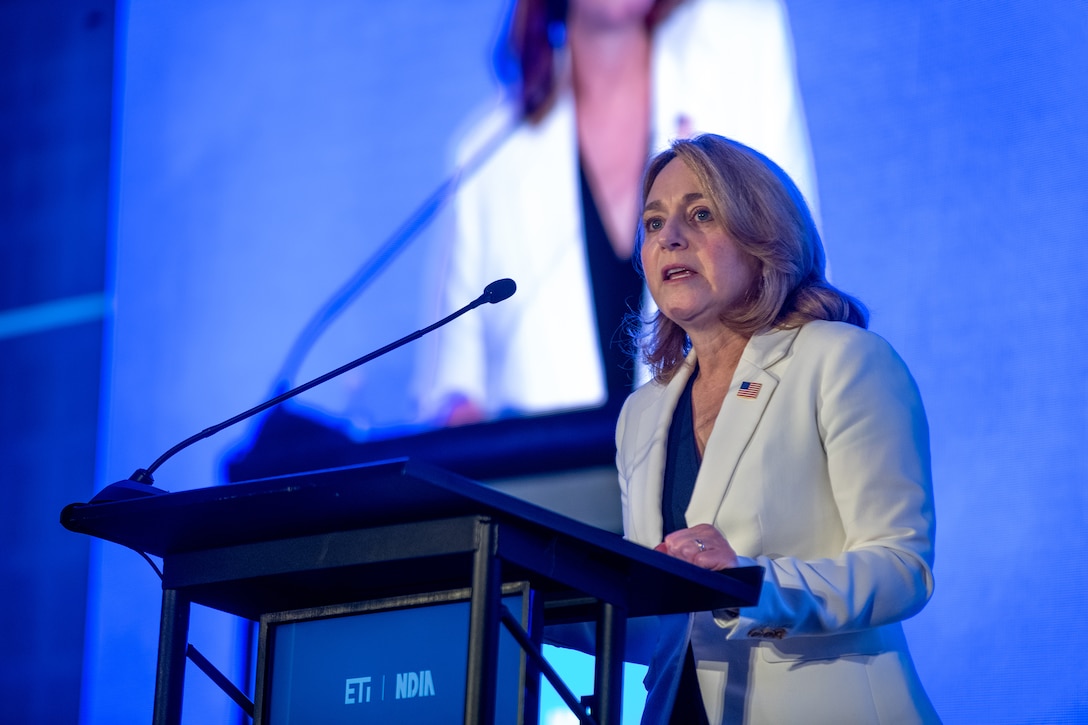 A person speaks from behind a lectern in front of a large screen.